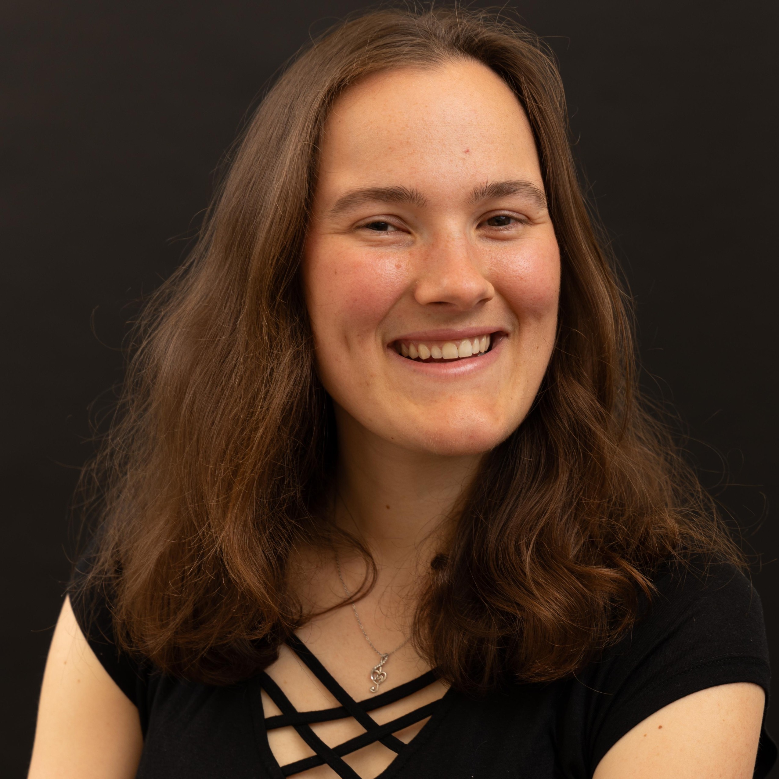 Photo portrait of a woman. She is smiling. She has light brown hair and she is wearing a black t-shirt. She is crossing her arms. She looks professional.