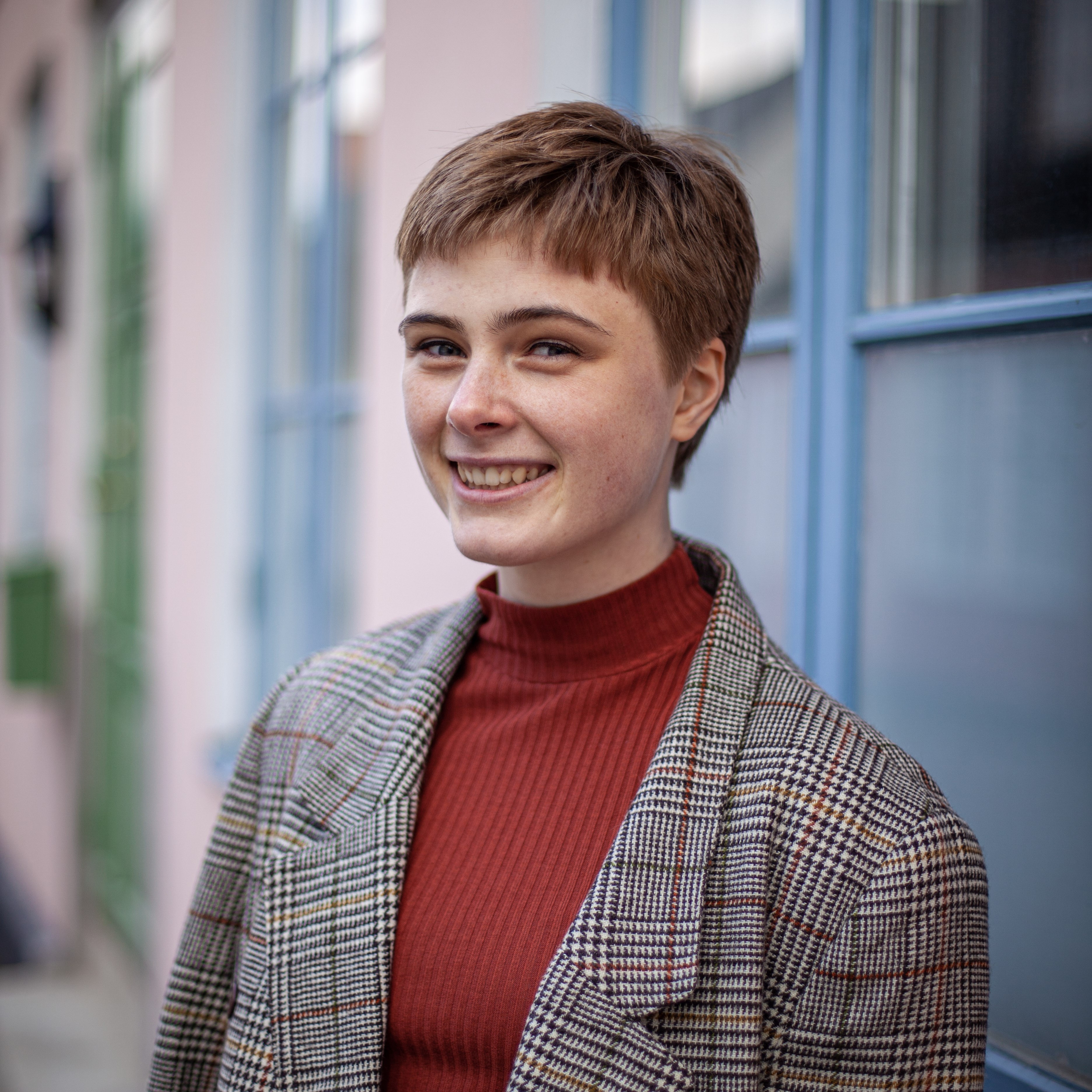 Headshot portrait of a woman, she is smiling, wearing a grey vest and a red sweater.